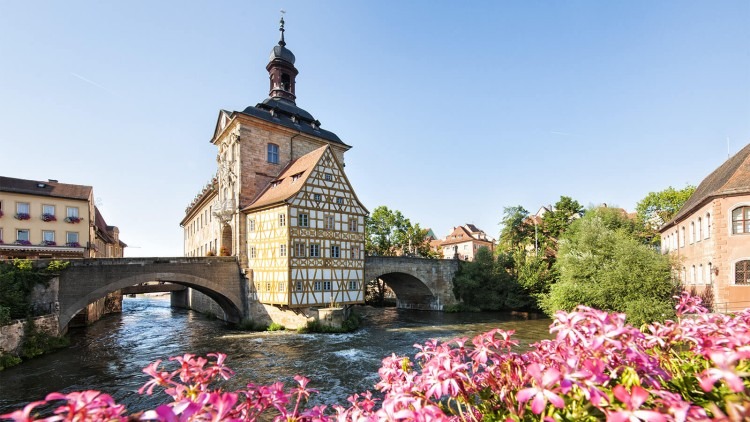 Historic building in Northern Bavaria with a bridge over water and flowers in the foreground