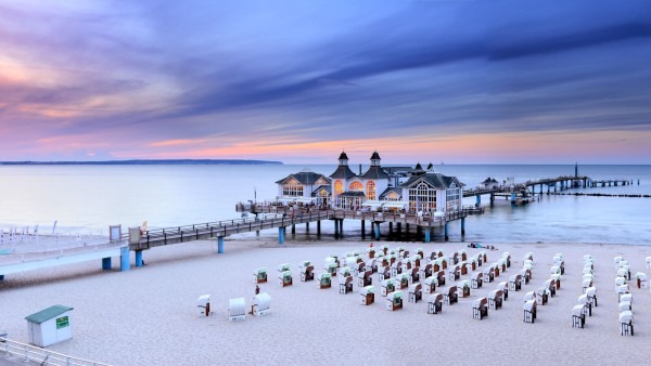 Beach with wooden pier and people on beach chairs at sunset